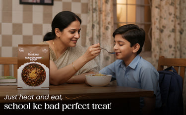 Woman feeding a child at a table with a box of food in the foreground.