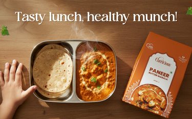 Lunch box with paneer butter masala and roti, accompanied by a packet of the dish on a wooden surface.