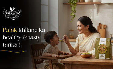 Woman feeding a child at a table with a box of food packaging in the background.