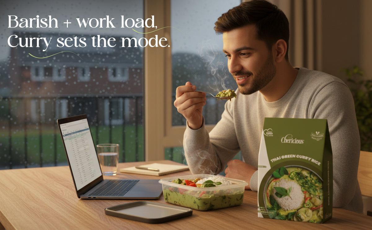 Man eating a meal with a laptop and smartphone on a table, Cherishin curry box visible