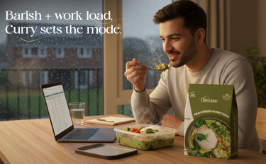 Man eating a meal with a laptop and smartphone on a table, Cherishin curry box visible