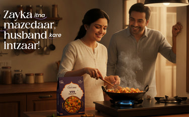 Man and woman cooking together in a kitchen with a box of Arora's Veg on the counter.