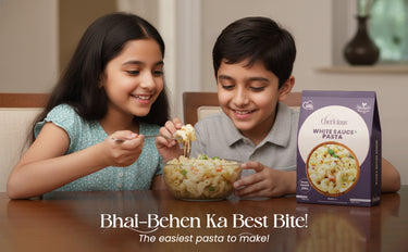 Two children eating pasta from a bowl with a box of Cheekies pasta in the background.