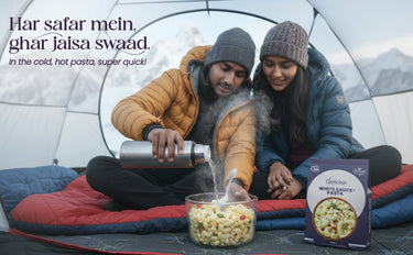 Two people sitting inside a tent, preparing pasta with a box of sauce in front of them.